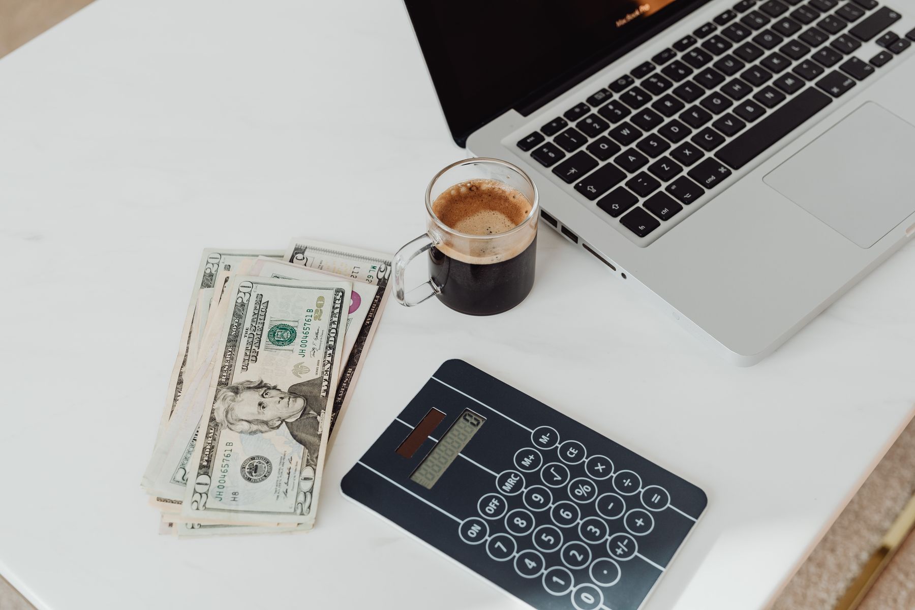 A laptop, a coffee, and a calculator on a white marble desk