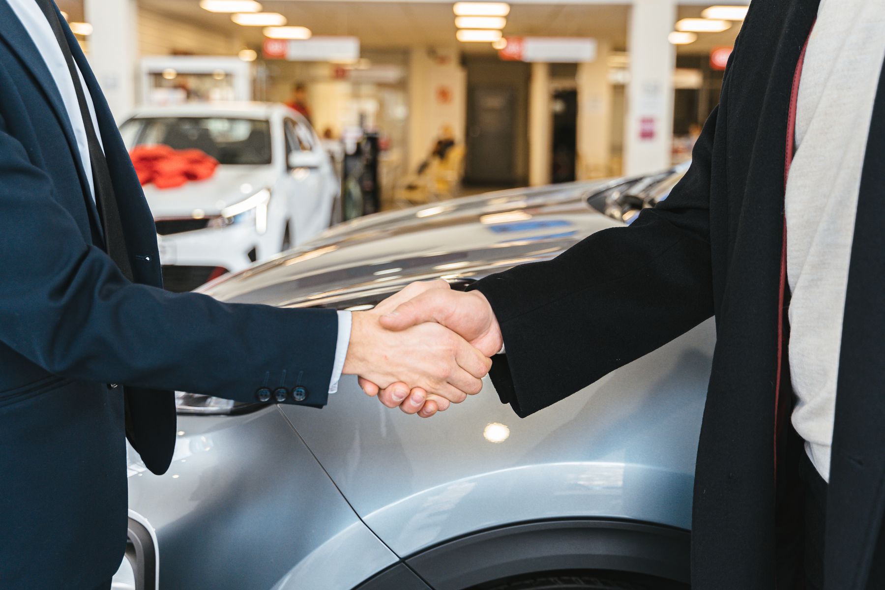 A handshake over the hood of a car in a showroom